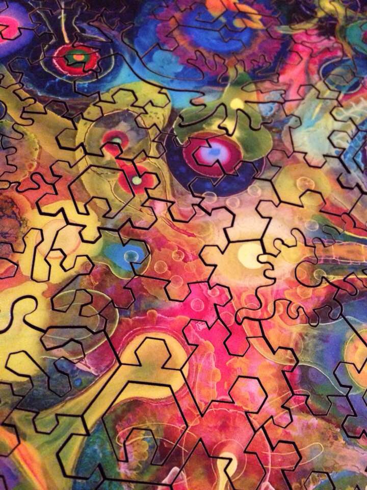 Wooden jigsaw pieces that look like gears are joined together showing a psychedelic image that depicts nothing recognizable
