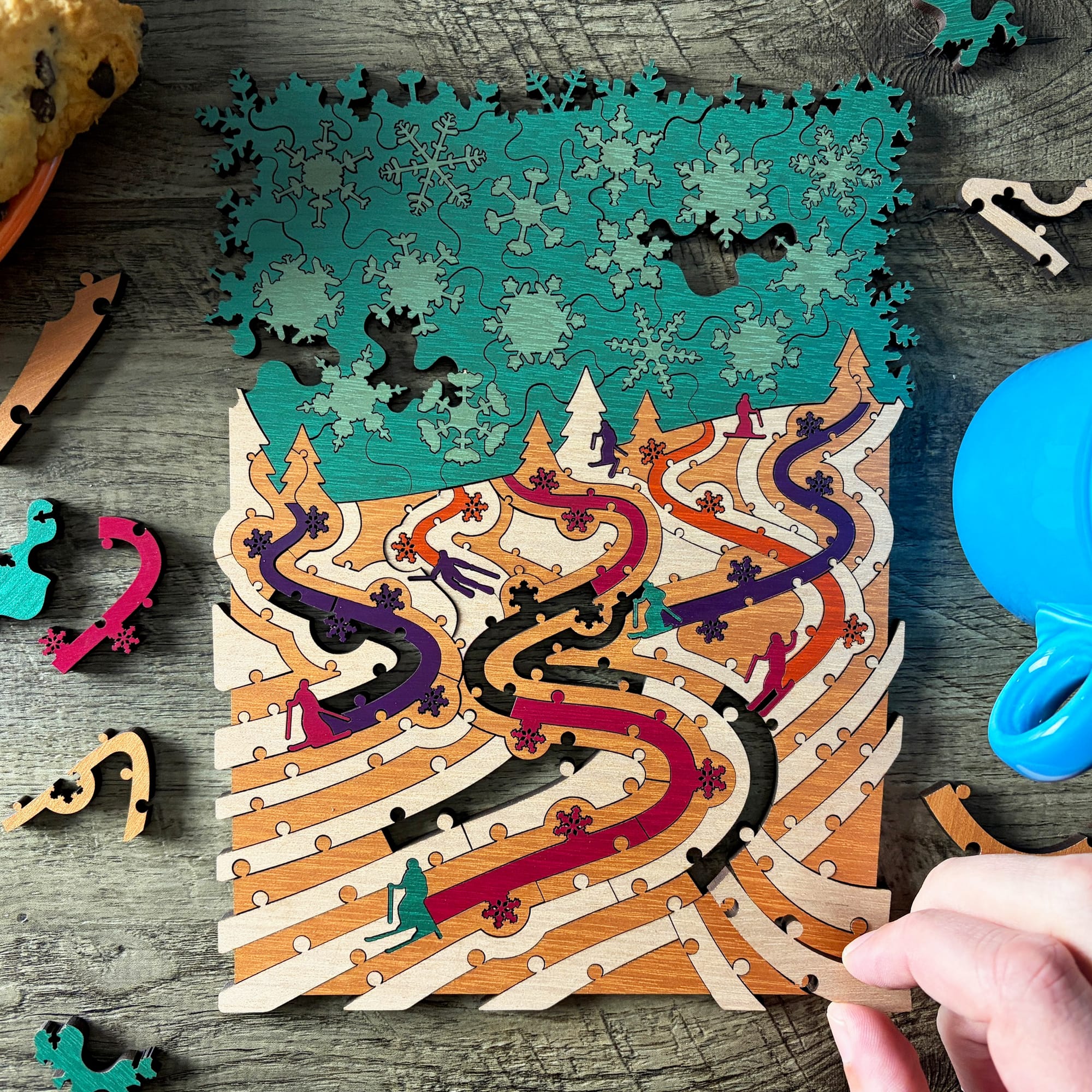 A wooden puzzle showing giant snowflakes in the sky above skiers who have colorful trails in their wake
