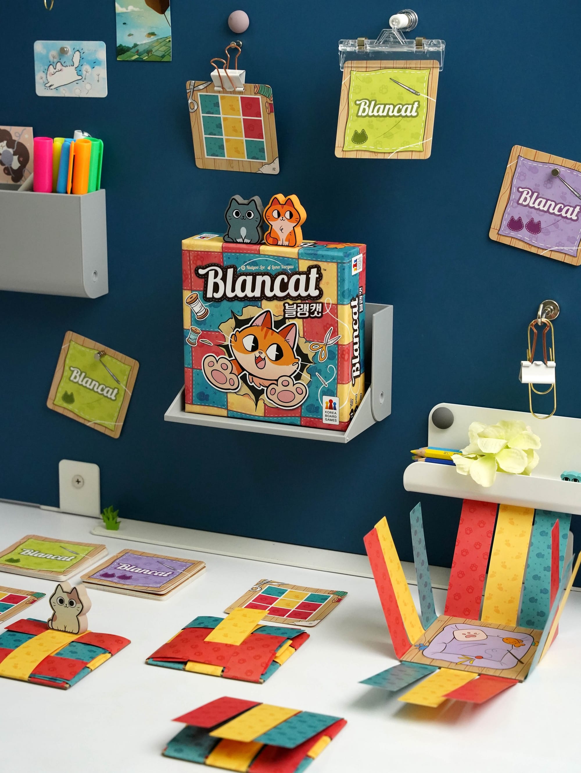 The front cover of Blancat and examples of gameplay, with a square bed having three "cloths" along each edge that will be folded on top