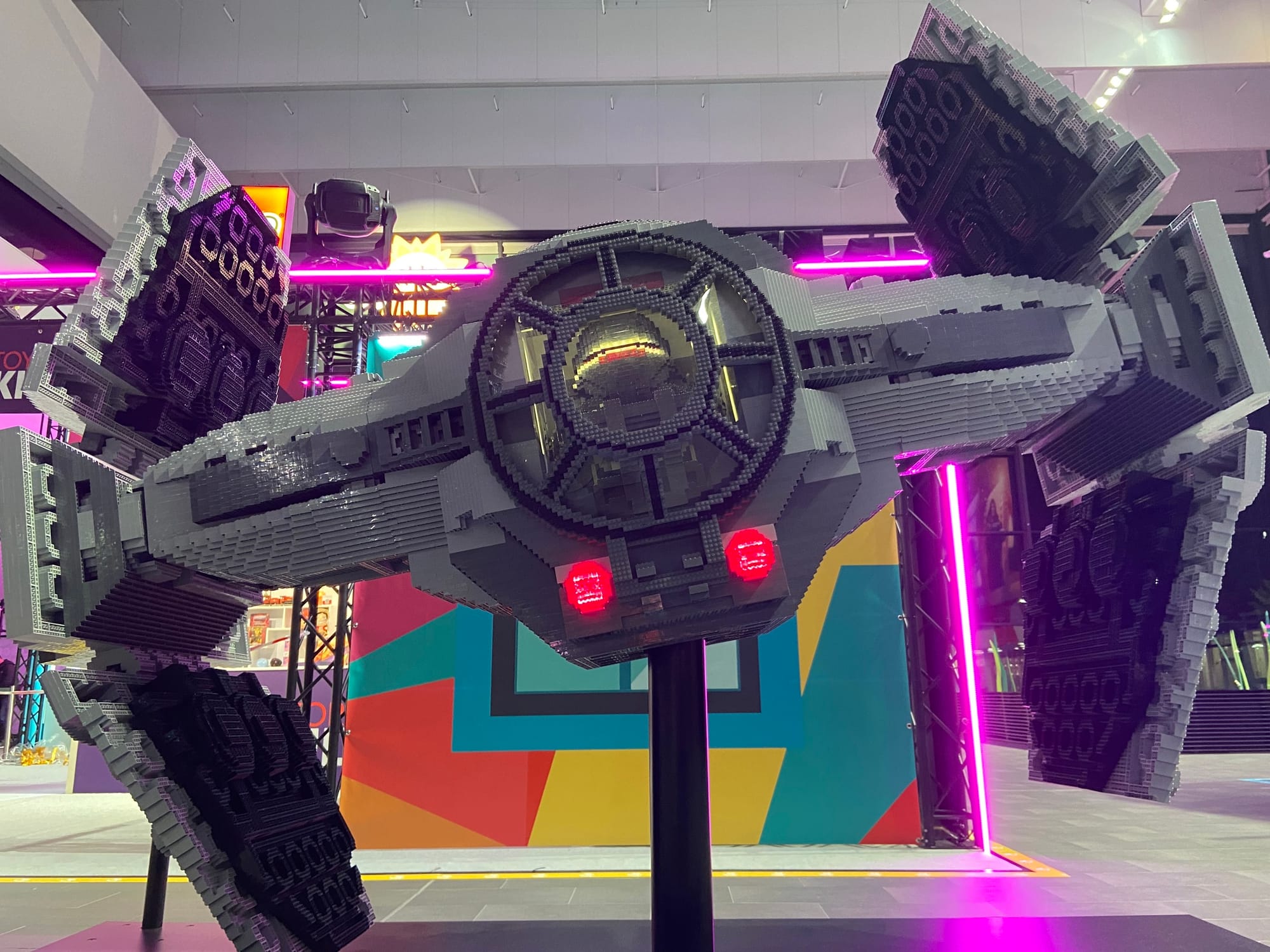 A human-sized LEGO TIE fighter on a giant pole in front of a neon-lit convention booth