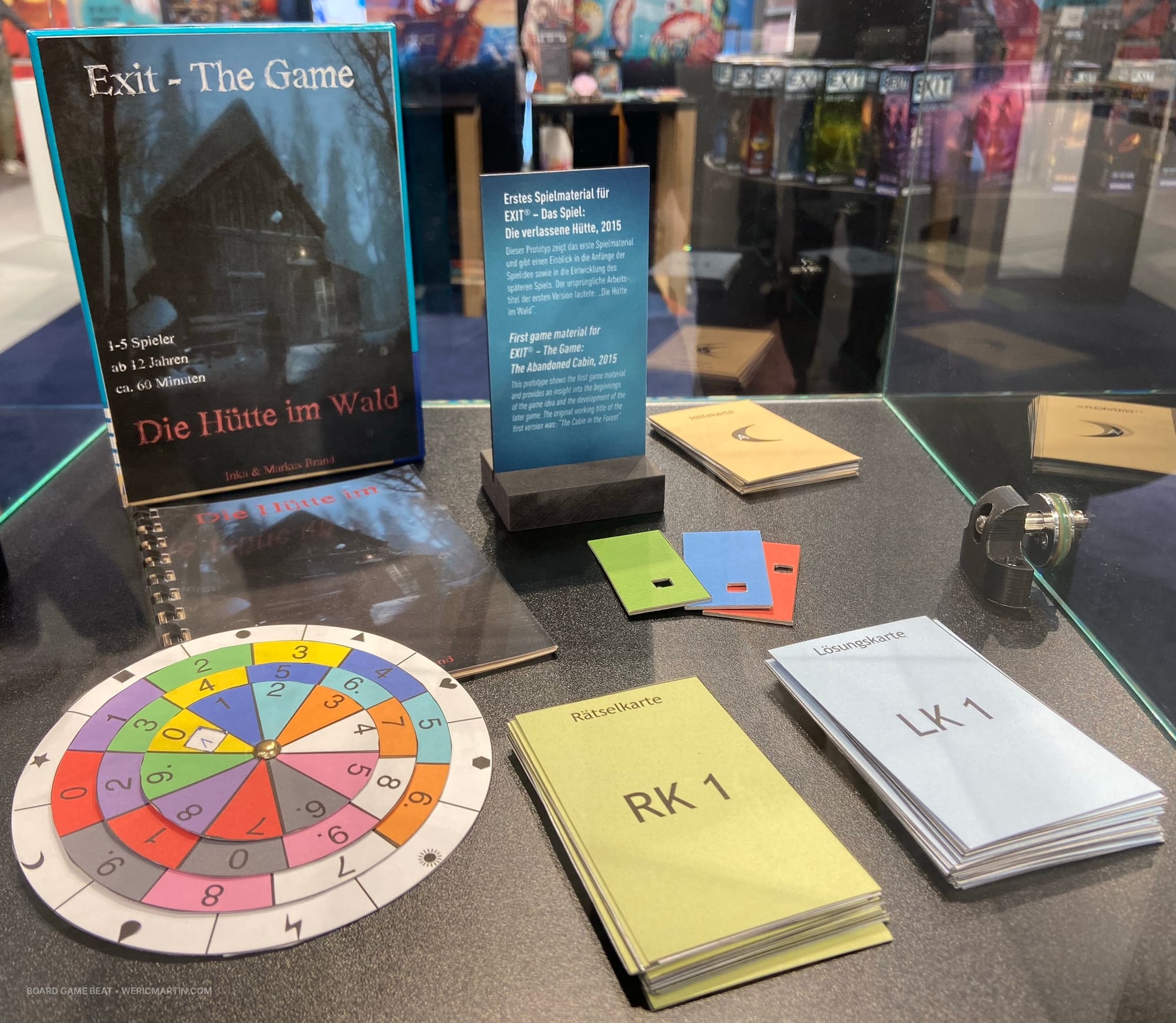 A homemade box for EXIT: The Game is standing behind a booklet, a code wheel (with four colored circles pinned together and spinning independently), two decks of cards, and other components