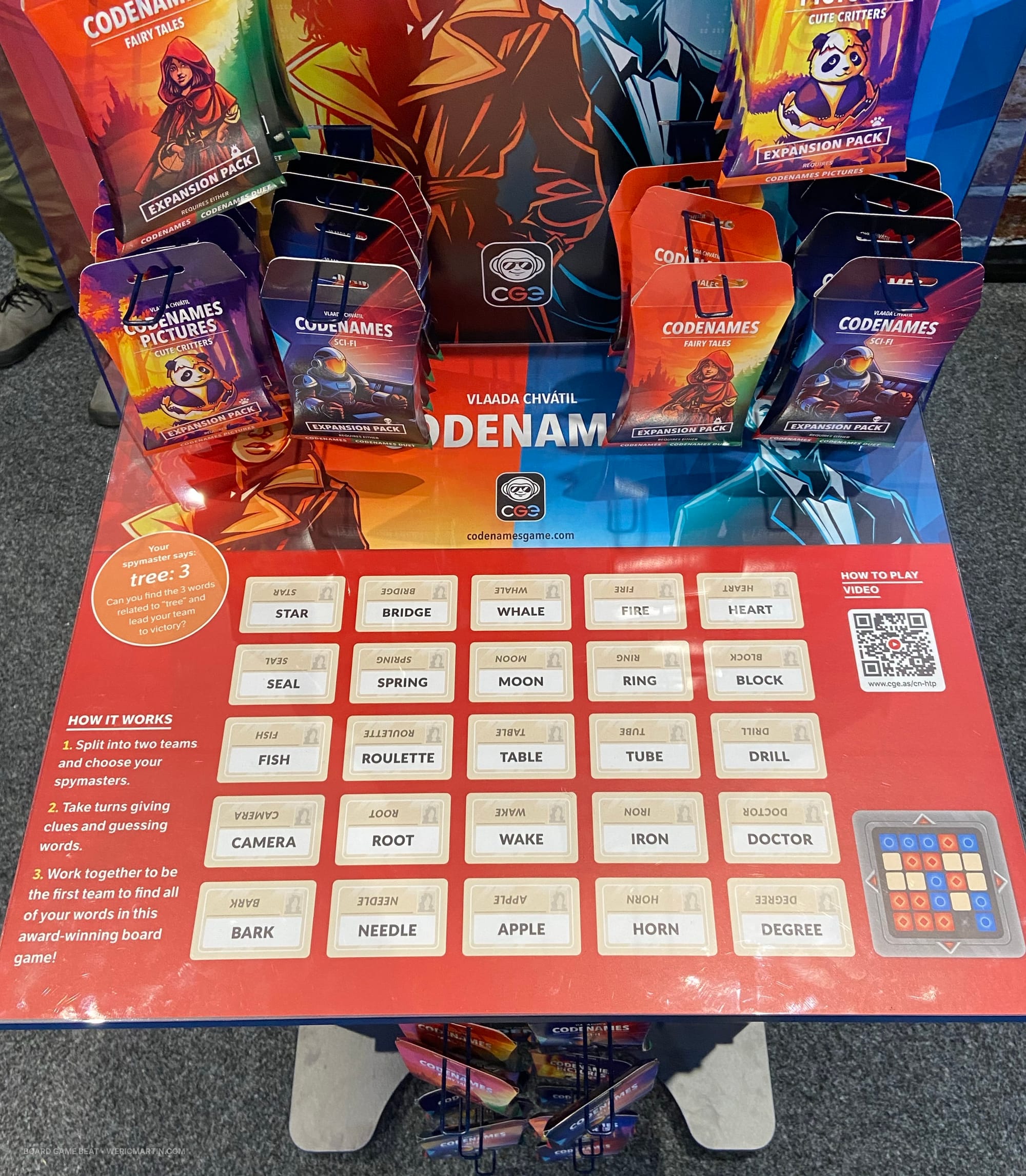 The top of the Codenames retail display, which includes a QR code for the rules, a sample layout of cards, and a written explanation of how to play