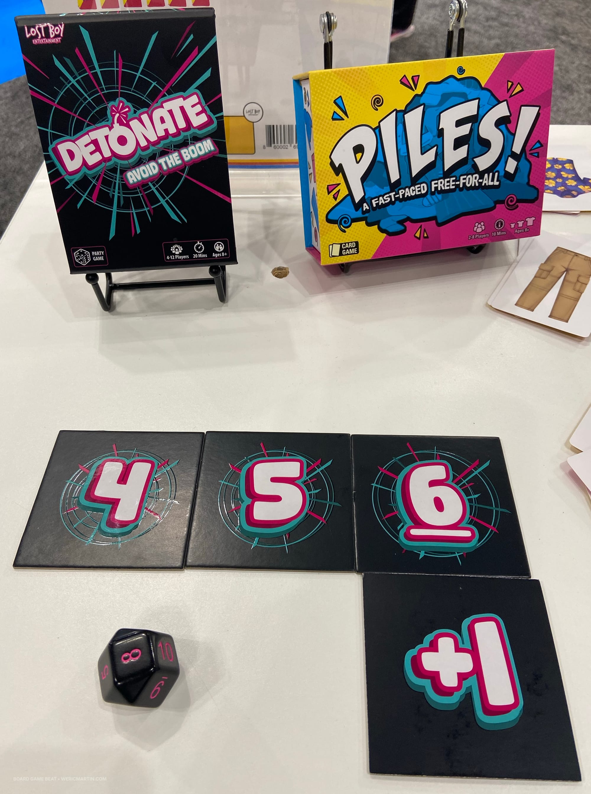 Two game boxes — Detonate and Piles — are at the top of the image, with tiles numbered 4-6 below, along with a +1 tile and a ten-sided die