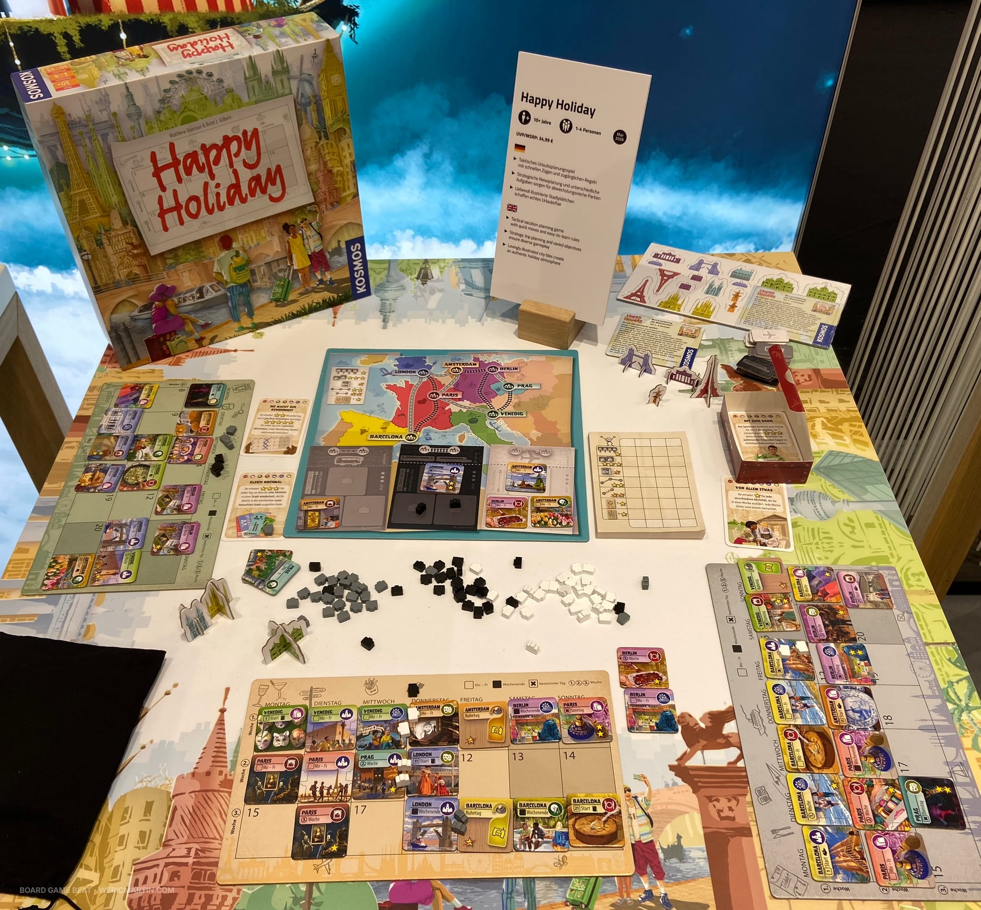 Components for the game Happy Holiday, which includes a three-week calendar game board for each player, city tiles, and suitcases in three colors