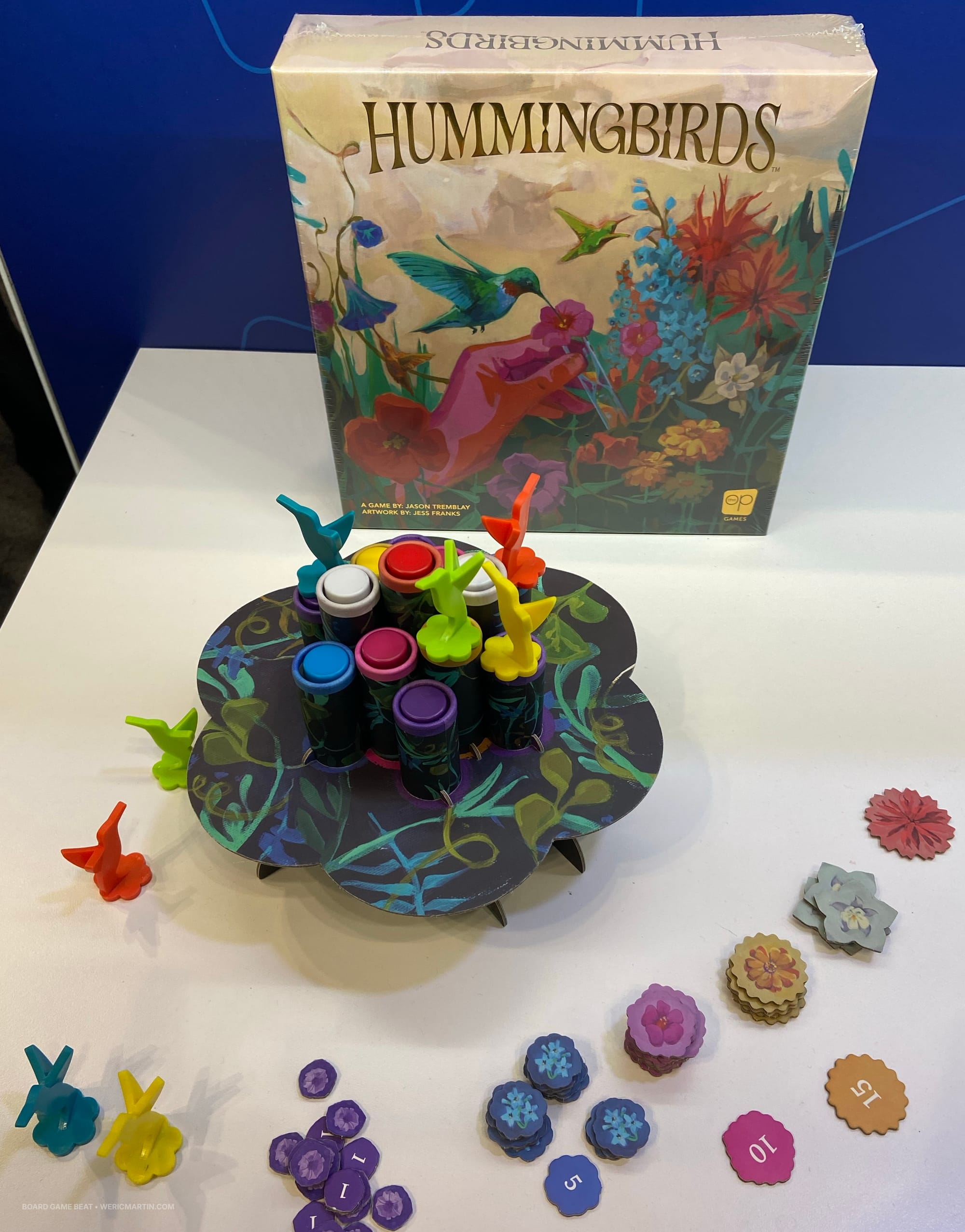 Game box for Hummingbirds behind a cardboard display that features thirteen cardboard tubes, each holding a sand timer