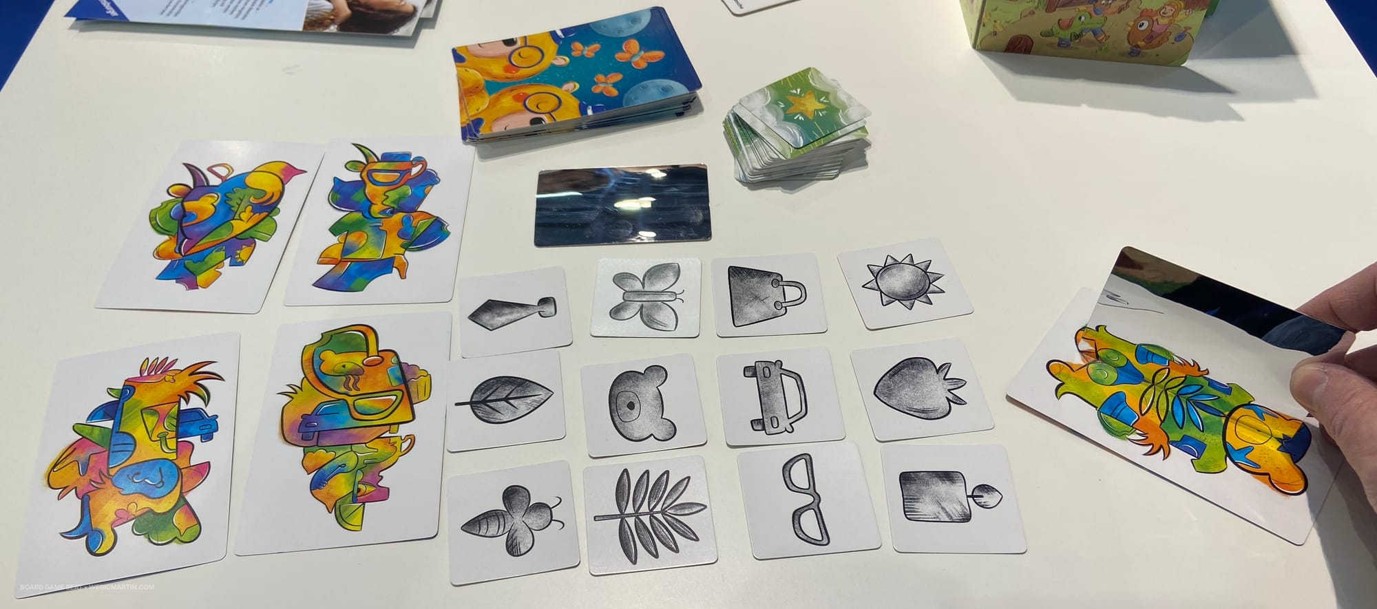 A hand holds a mirror next to a colored card so that a group of ovals are duplicated to look like a tree branch