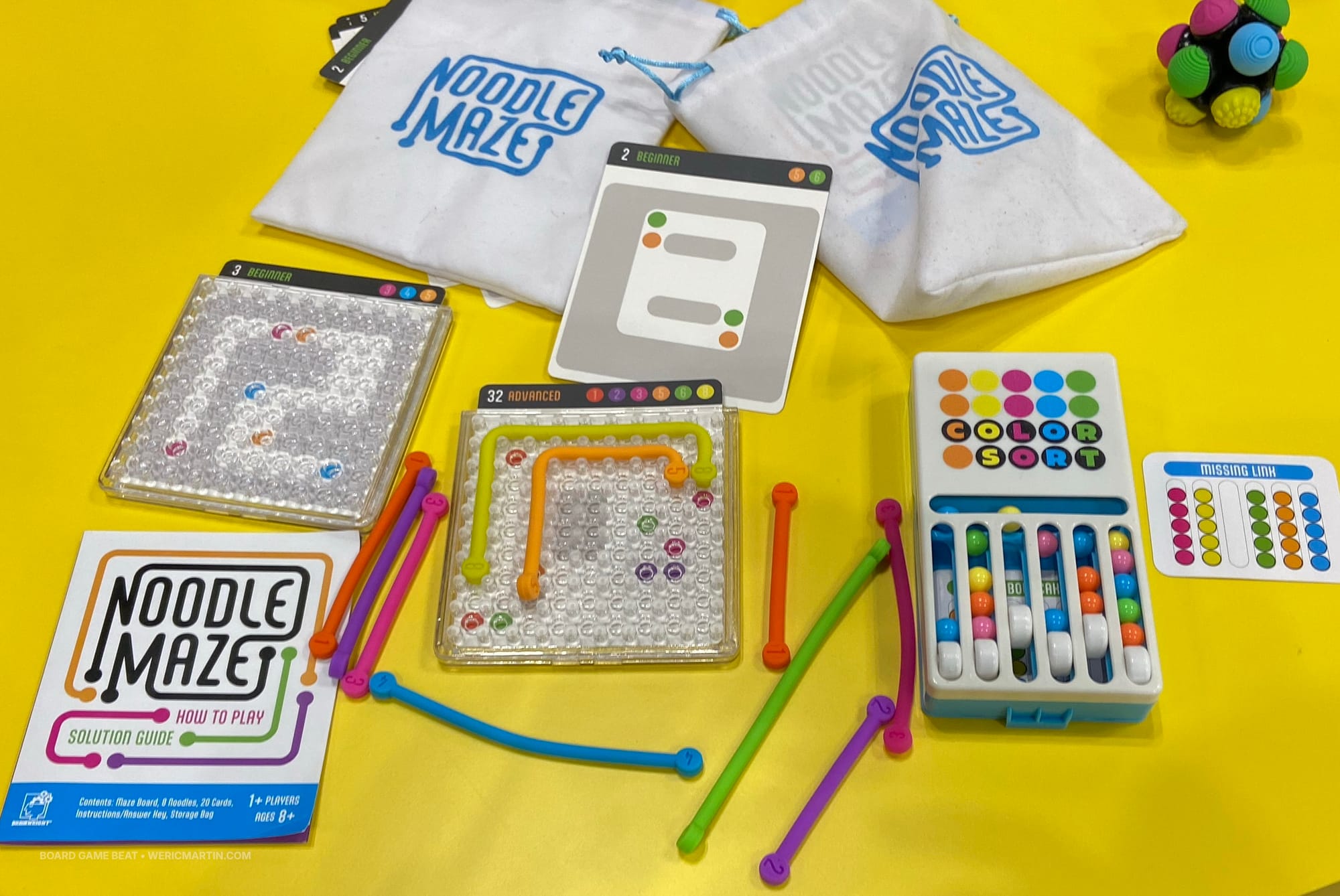 A plastic grid covered with pegs has a couple of plastic "noodles" snaking through the pegs; more noodles are on the side of the grid