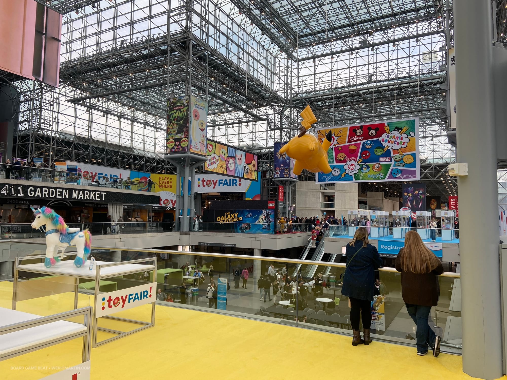 A view from inside the Jacob K. Javits Convention Center, showing lots of Toy Fair signage and a few exhibits outside the show