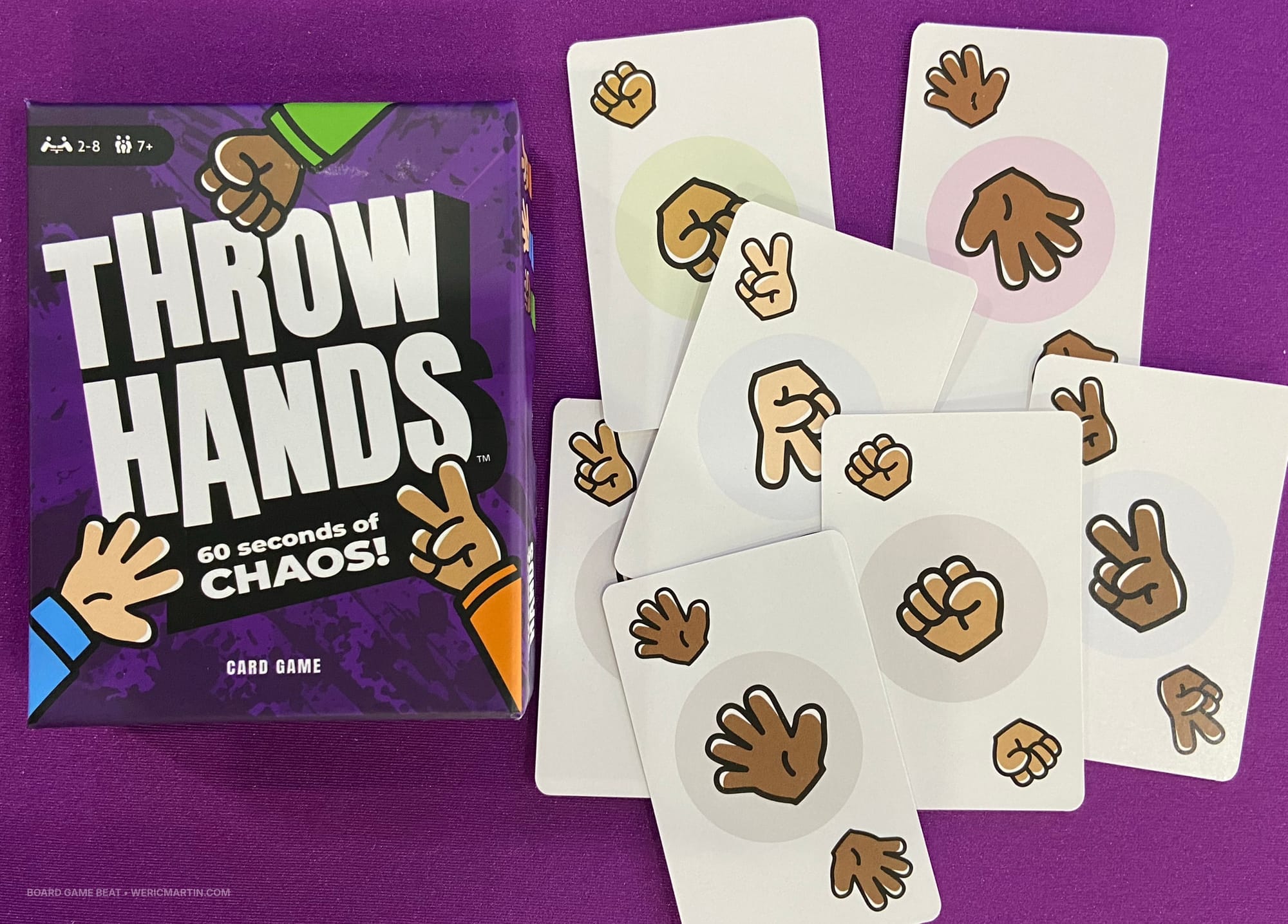 The game box for Throw Hands is next to sample cards, which show hands exhibiting rock, paper, and scissors symbols