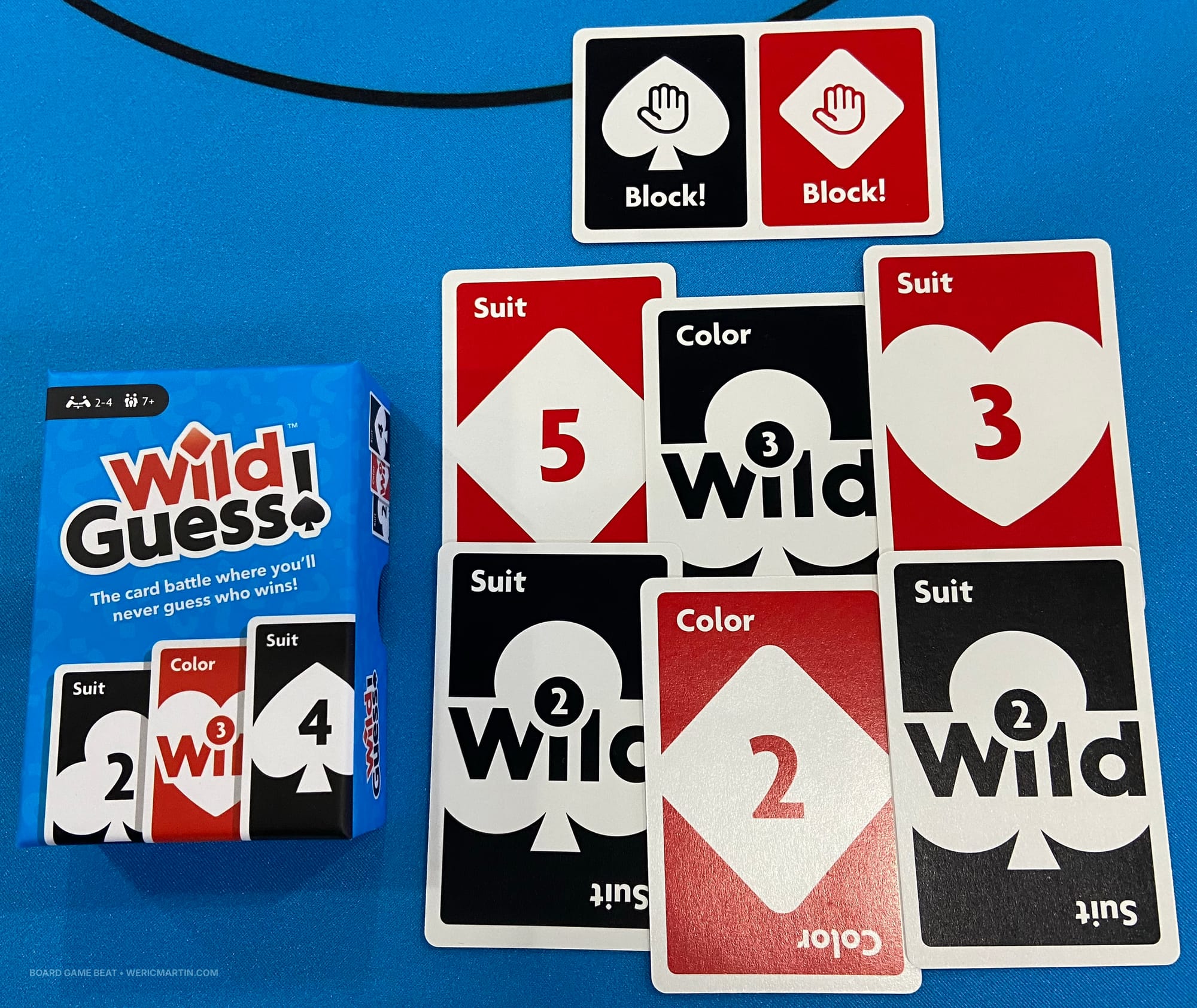 The box for Wild Guess! along with sample cards in red and black with the traditional card suits
